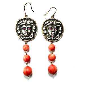 May include: Gold earrings with a silver face pendant and coral beads.