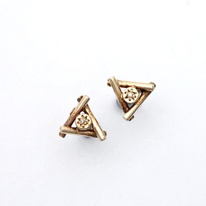 May include: A pair of gold triangle earrings with a small diamond in the center of each triangle.