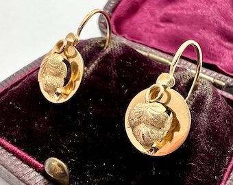 May include: A pair of gold earrings with a detailed floral design. The earrings are hanging from a velvet box.