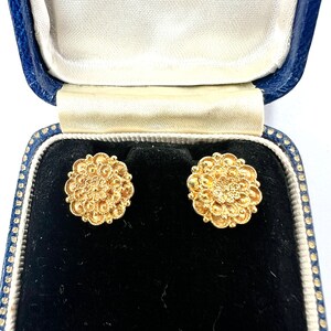 以下が含まれることがあります： 花柄のデザインの金色のイヤリングのペア。イヤリングは青いベルベットのジュエリーボックスに入っています。