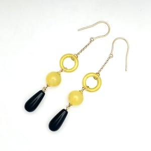 May include: A pair of gold dangle earrings with yellow and black beads. The earrings feature a circle bead and a round bead.