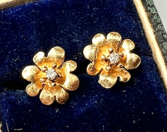 以下が含まれることがあります： 花の形をした金のイヤリングのペア。それぞれの金のフラワーモチーフの中央にダイヤモンドが1つずつセットされています。