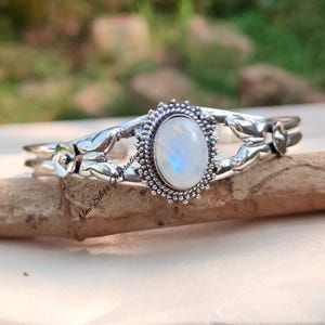 May include: A silver bracelet with a moonstone oval cabochon set in a floral design. The bracelet is open and adjustable.