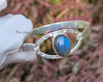 May include: Silver bracelet featuring a blue labradorite gemstone set in an eye-shaped design. The bracelet is hammered and has a textured finish. "New Silver Generation" is written on the bracelet.