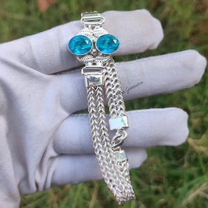 May include: A silver bracelet with a chain link design and two blue oval-shaped gemstones. The bracelet has a clasp closure.
