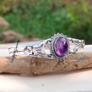 May include: A silver bracelet with a purple amethyst gemstone set in a floral design. The bracelet features butterfly and flower accents.
