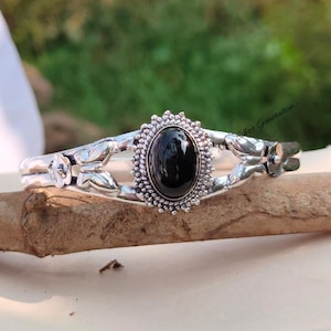 May include: A silver bracelet with a black gemstone set in a floral design. The bracelet features two butterfly accents and the text "New Silver Generation".