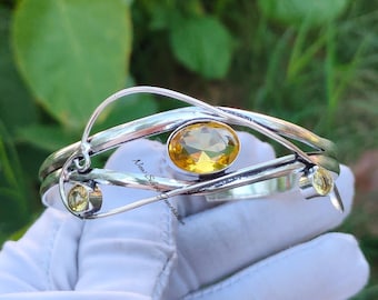 May include: A silver bangle bracelet with a yellow gemstone and two smaller yellow gemstones. The bracelet has a twisted design and is made of sterling silver.