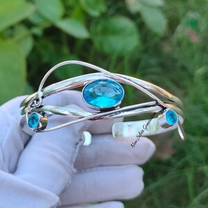 Peut inclure: Bracelet en argent avec trois accents de pierres précieuses bleues. Le bracelet est fait de fil d'argent torsadé et présente une plus grande pierre précieuse bleue de forme ovale au centre.