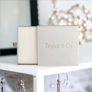 Puede incluir: Una caja de regalo blanca con una tapa texturizada y el texto "Taylor & Co. Personalised Gifts" en la parte delantera.
