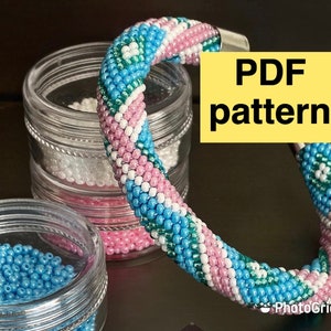 May include: A beaded bracelet with a blue, pink, and green color pattern. The bracelet is coiled and resting on a clear container. The text "PDF pattern" is on a yellow background.