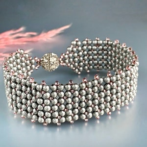 Peut inclure: Un bracelet en perles argentées et roses avec un fermoir argenté. Le bracelet est composé de petites perles rondes disposées en un motif géométrique.