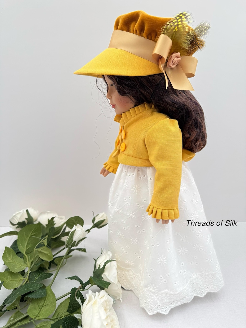 May include: A doll wearing a yellow hat with a wide brim and a matching yellow jacket with decorative buttons. The doll is also wearing a white eyelet skirt. The hat is adorned with a bow and feathers. The text "Threads of Silk" is visible.