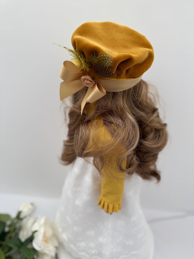 May include: Mustard yellow beret with a satin ribbon and a small flower accent. The beret is adorned with feathers and is set on a head of wavy, light brown hair. The beret is part of a vintage-inspired fashion ensemble.