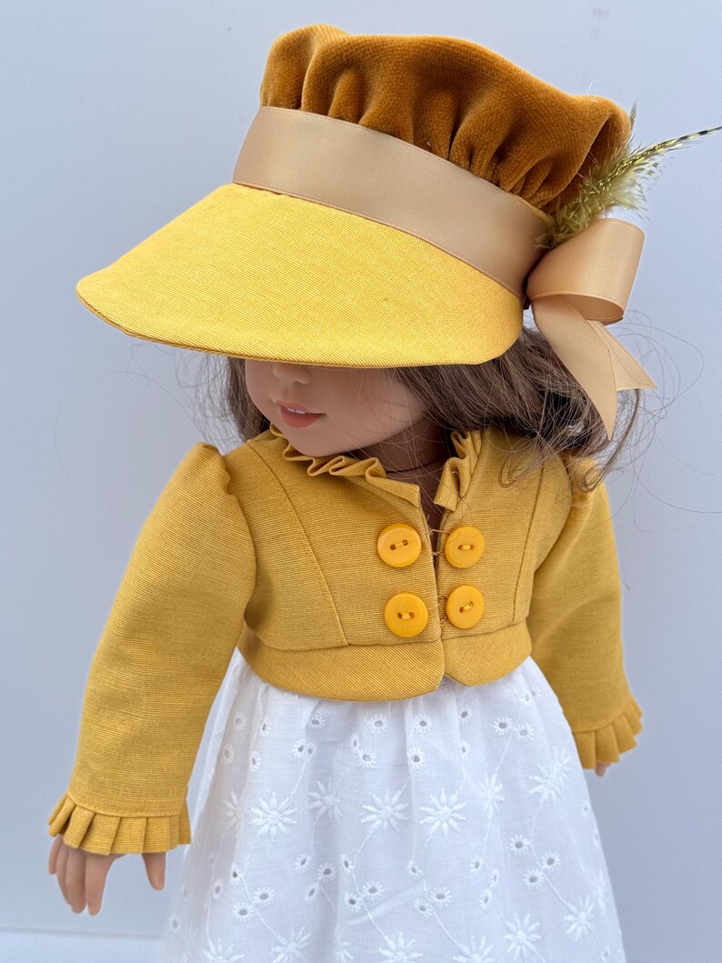 May include: A doll wearing a yellow sun visor with a brown velvet crown and a matching bow. The doll is also wearing a yellow jacket with four round buttons and a white eyelet dress. The outfit is a vintage style.