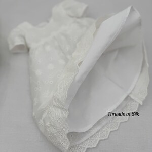 Puede incluir: Vestido blanco de ojal con mangas cortas y dobladillo de encaje festoneado. El vestido presenta un delicado bordado floral y el texto "Threads of Silk". Una prenda cl&aacute;sica y elegante.