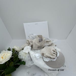 Puede incluir: Una chaqueta beige con estampado floral y un sombrero a juego con ala. El conjunto se acompa&ntilde;a de detalles florales blancos y una tela blanca con dise&ntilde;o floral. El texto "Threads of Silk" es visible.