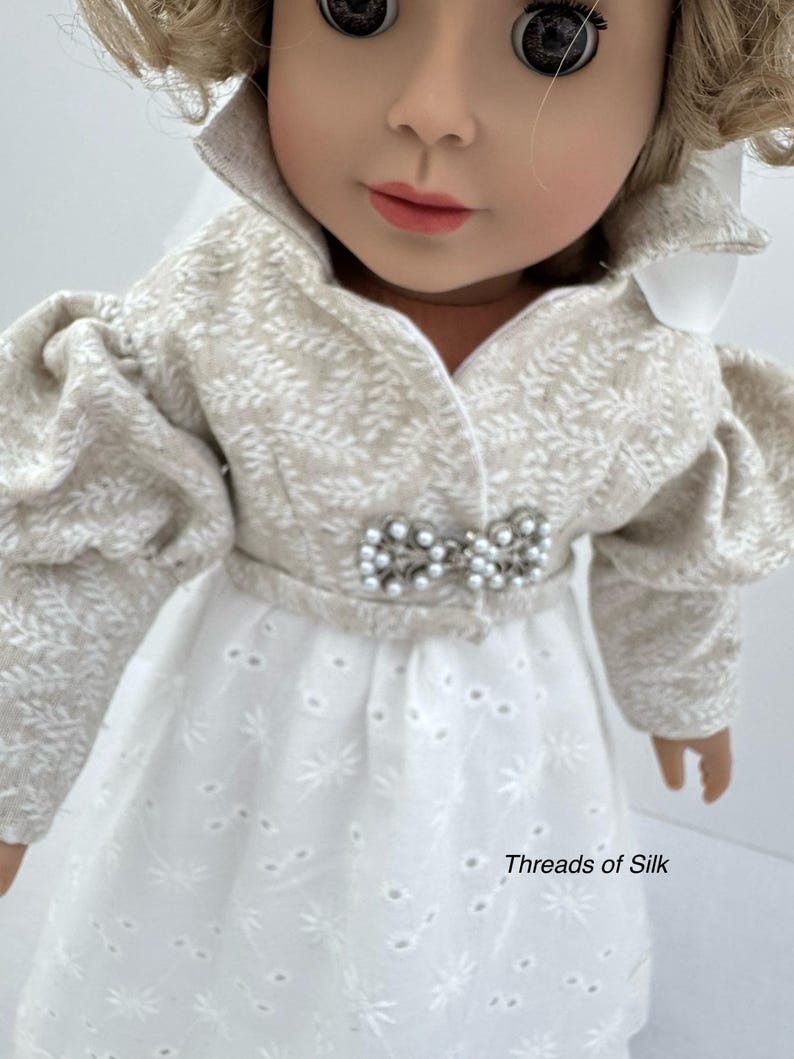 Puede incluir: Una mu&ntilde;eca vestida con una chaqueta color crema con estampado de hojas y un vestido calado blanco. La chaqueta tiene mangas abullonadas y una broche de perlas. El vestido tiene un dise&ntilde;o calado floral. El texto "Threads of Silk" es visible.
