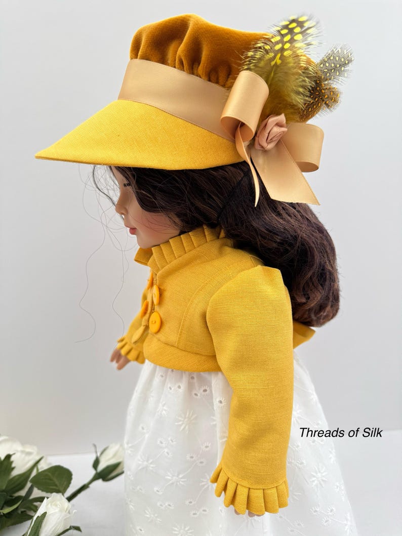May include: A doll wearing a yellow hat with a wide brim, a matching jacket, and a white eyelet dress. The hat is adorned with a bow, feathers, and a small flower. The jacket has decorative buttons and ruffled cuffs. The text "Threads of Silk" is visible.