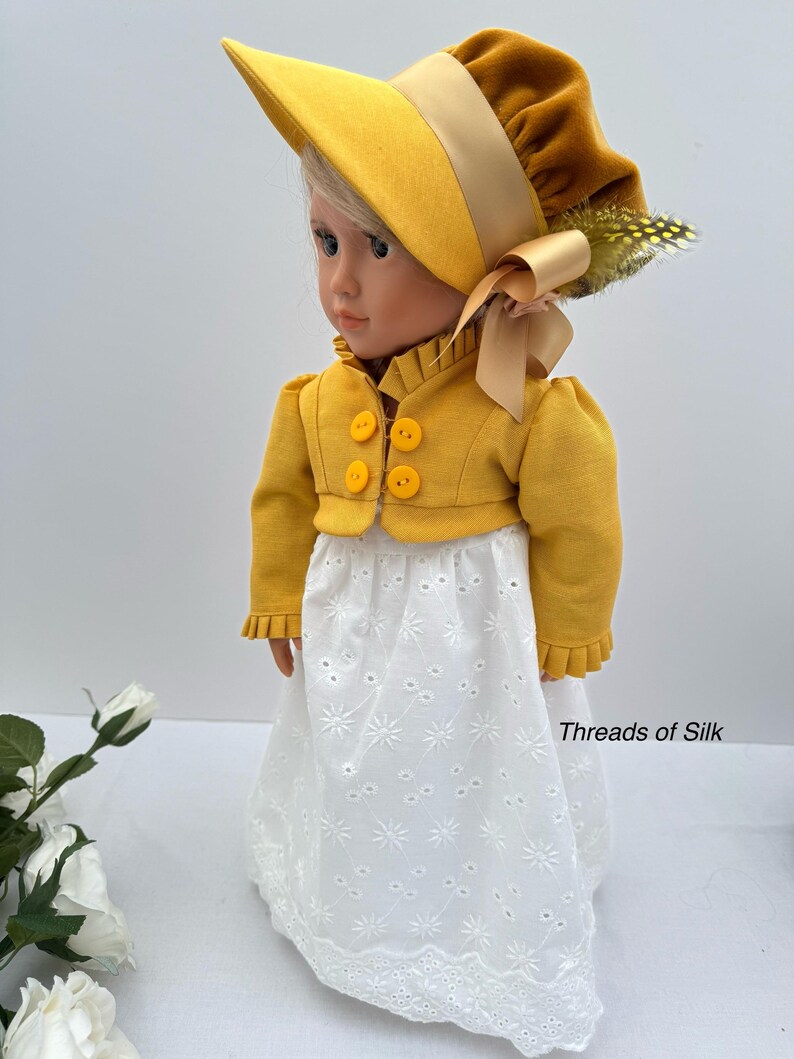 May include: A doll wearing a yellow bonnet, jacket, and white eyelet skirt. The bonnet has a wide brim and is adorned with a ribbon and feather. The jacket has three yellow buttons. The skirt has a floral pattern. The text "Threads of Silk" is visible.