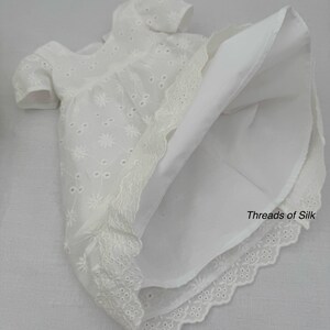 Puede incluir: Vestido blanco de ojal con mangas cortas y ribete de encaje festoneado. El vestido presenta un estampado floral y una falda amplia. El texto "Threads of Silk" es visible.