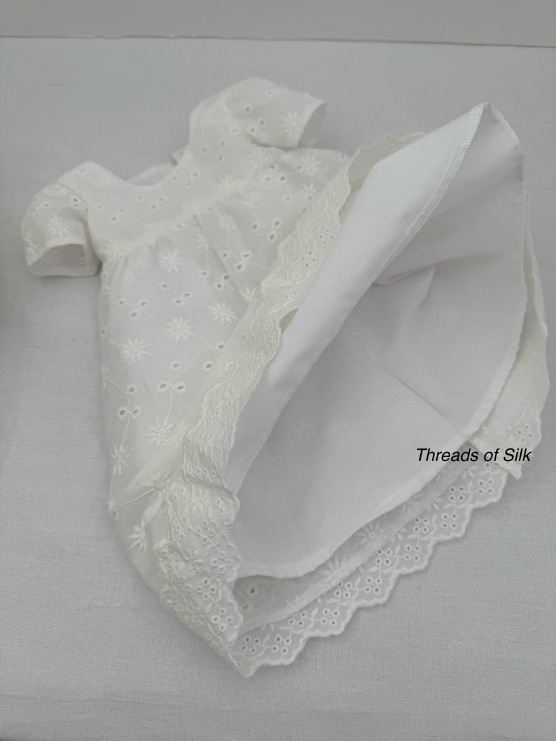 Puede incluir: Vestido blanco de ojal con mangas cortas y ribete de encaje festoneado. El vestido presenta un estampado floral y una falda amplia. El texto "Threads of Silk" es visible.