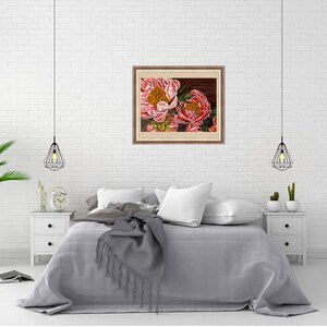 May include: A framed painting of two pink peonies with yellow centers. The painting is hanging on a white brick wall above a gray bed with white pillows and a gray throw blanket.
