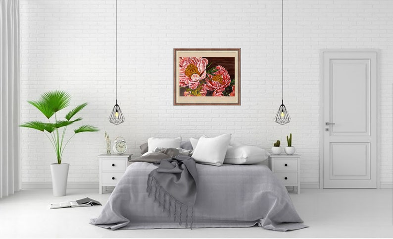 May include: A framed painting of two pink peonies with yellow centers. The painting is hanging on a white brick wall above a gray bed with white pillows and a gray throw blanket.