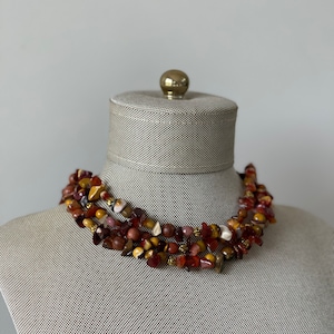 May include: A multi-strand necklace made of brown, red, and gold gemstone beads. The necklace is layered and has a chunky, rustic look.