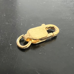 Op de afbeelding: Gouden metalen sluiting met een veerbelaste sluiting. De sluiting heeft een gladde, gepolijste afwerking en een kleine ring aan één uiteinde.