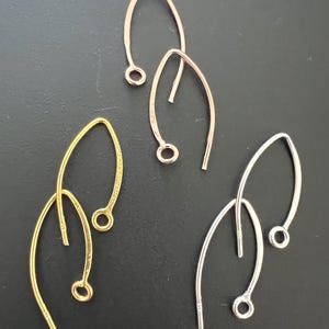 Könnte beinhalten: Drei Paar Ohrhaken in Gold, Silber und Roségold. Die Haken sind aus Metall und haben ein schlichtes, elegantes Design.