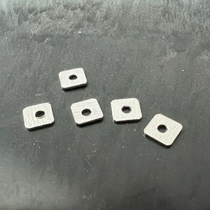 Può includere: Cinque quadrati in metallo argentato con un foro al centro. I quadrati sono disposti a forma di piramide.