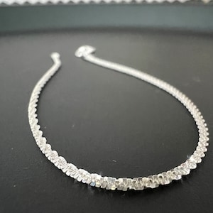 Könnte beinhalten: Eine silberne Kettenkette mit einem zarten, strukturierten Design. Die Kette besteht aus kleinen, quadratischen Gliedern, die miteinander verbunden sind, um ein durchgehendes Muster zu bilden.