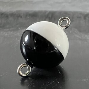 May include: Black and white round buoy with two silver metal rings. The buoy is half black and half white.