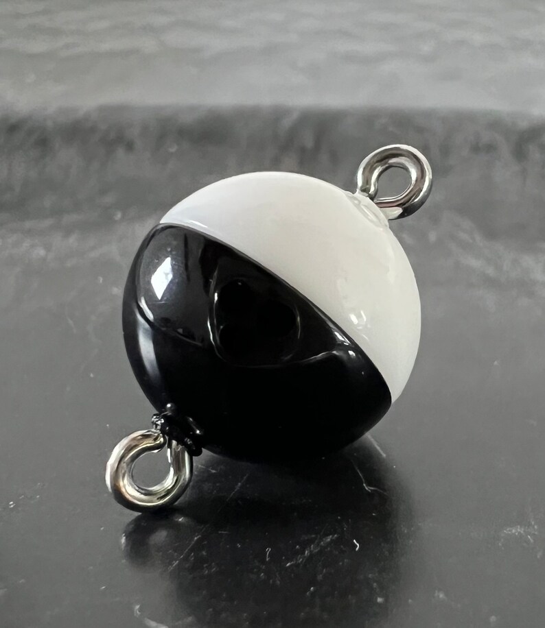 May include: Black and white round buoy with two silver metal rings. The buoy is half black and half white.