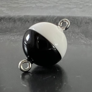 May include: A black and white round bead with a silver metal loop on each side. The bead is half black and half white.