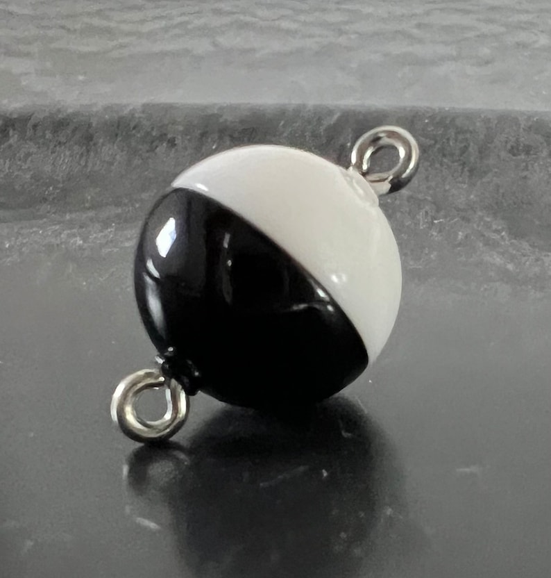 May include: A black and white round bead with a silver metal loop on each side. The bead is half black and half white.