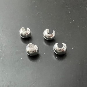 Puede incluir: Cuatro tapas de cuentas de metal plateado, cada una con una forma redondeada y una pequeña abertura. Las tapas están diseñadas para ser utilizadas para la elaboración de joyas u otros proyectos de artesanía.