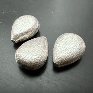 Może przedstawiać: Trzy srebrne koraliki w kształcie łzy z fakturowaną powierzchnią.