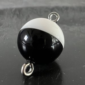 May include: Black and white round buoy with a silver metal loop on top and bottom.