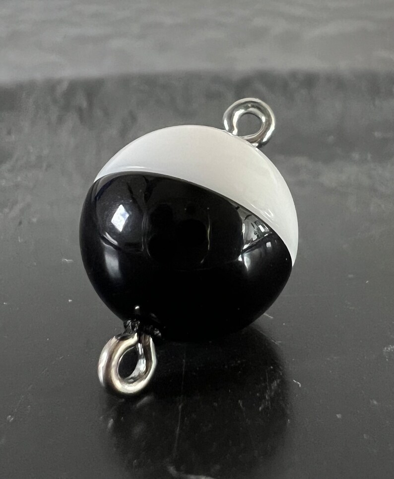 May include: Black and white round buoy with a silver metal loop on top and bottom.
