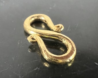 May include: A gold-colored metal S-shaped clasp or hook. The clasp is smooth and has a slightly textured surface.