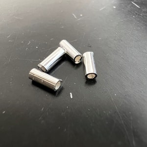 Op de afbeelding: Vier zilveren metalen gitaar-saddle-saddles. De saddles zijn cilindrisch en hebben een klein gaatje in het midden.