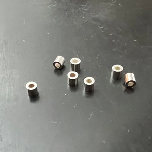 Könnte beinhalten: Sieben silberne Sprungringe, jeder mit einer kreisförmigen Öffnung, liegen verstreut auf einer dunkelgrauen Oberfläche.