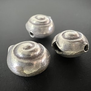 Może przedstawiać: Trzy srebrne metalowe koraliki ze spiralnym wzorem. Koraliki są gładkie i błyszczące.