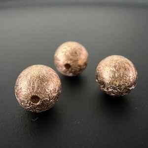 Może przedstawiać: Trzy okrągłe koraliki w kolorze złotym o fakturowanej powierzchni. Koraliki mają otwór w środku.
