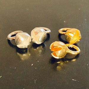 Pode incluir: Duas tampas de contas de metal prateado e dourado com uma abertura em forma de estrela. As tampas são projetadas para serem usadas como tampas finais para a fabricação de joias.