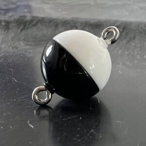 May include: A black and white glass sphere with a silver metal loop on each side. The sphere is half black and half white.