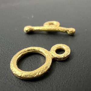 Pode incluir: Dois fechos de metal dourado, um com um laço redondo e o outro com uma barra reta.