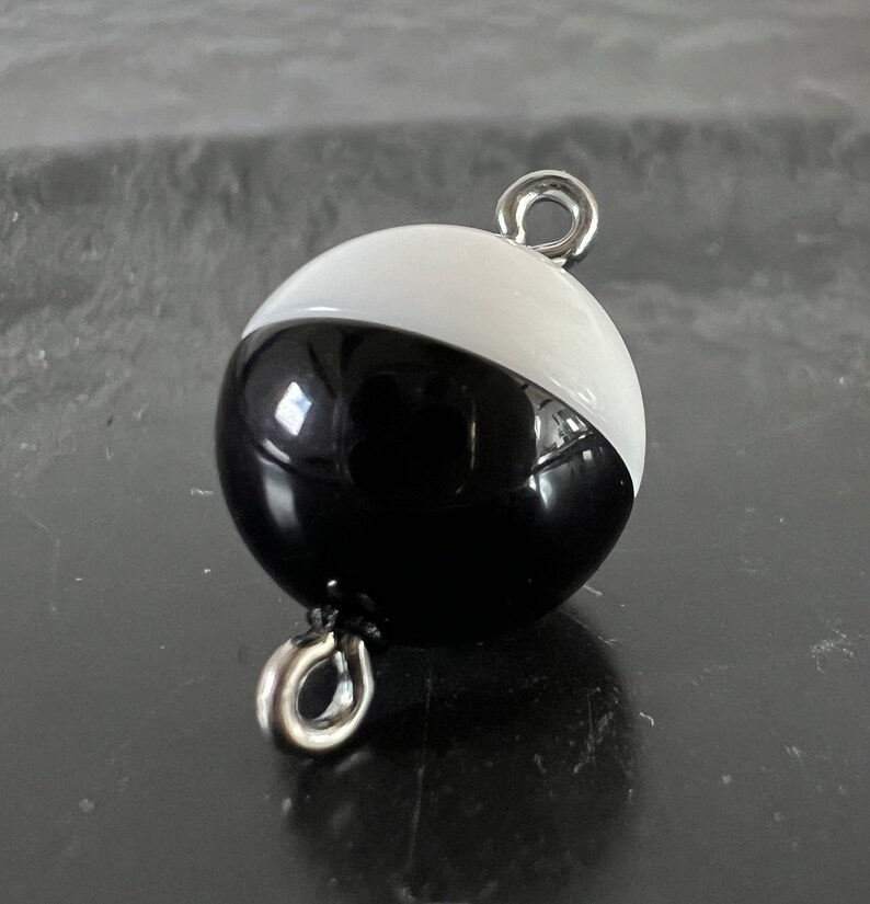 May include: A black and white round buoy with a silver loop on top. The buoy is half black and half white.